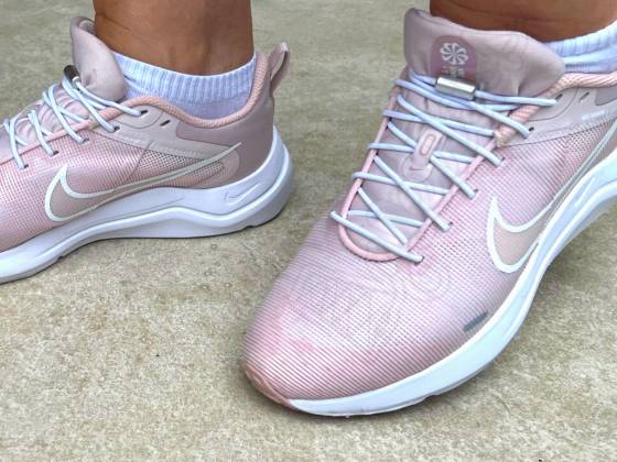 Een paar roze Nike hardloopschoenen voor dames met elastische veters. De schoenen zijn gemaakt van mesh en hebben een rubberen zool. De veters zijn gemaakt van een flexibel materiaal dat ervoor zorgt dat de schoenen gemakkelijk aan en uit te trekken zijn.